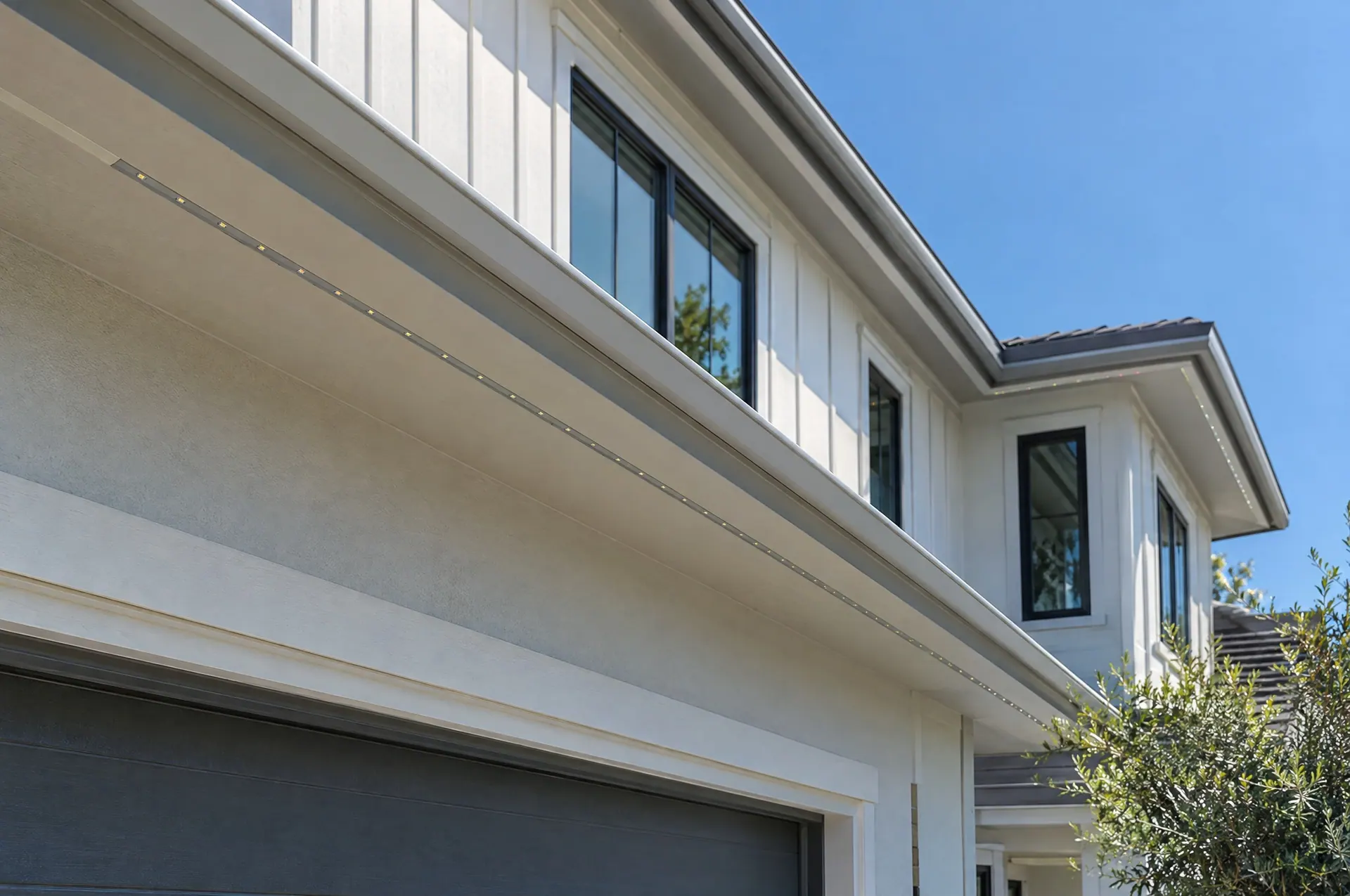 Slim permanent lighting channel mounted under a home's eave in daylight, painted to match the trim