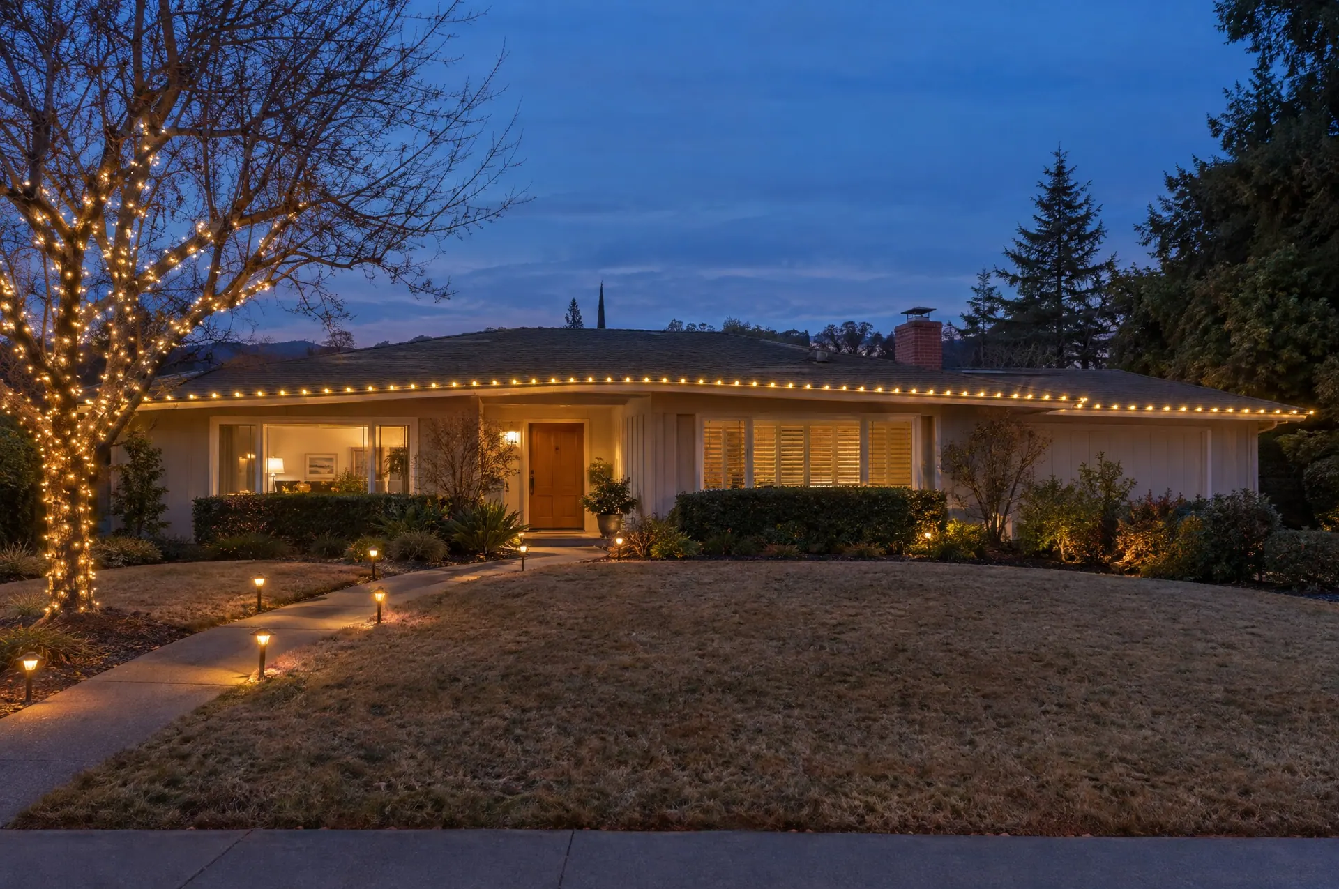 Single-story ranch home at blue hour with its long low roofline traced in warm white C9 lights and lit path lights